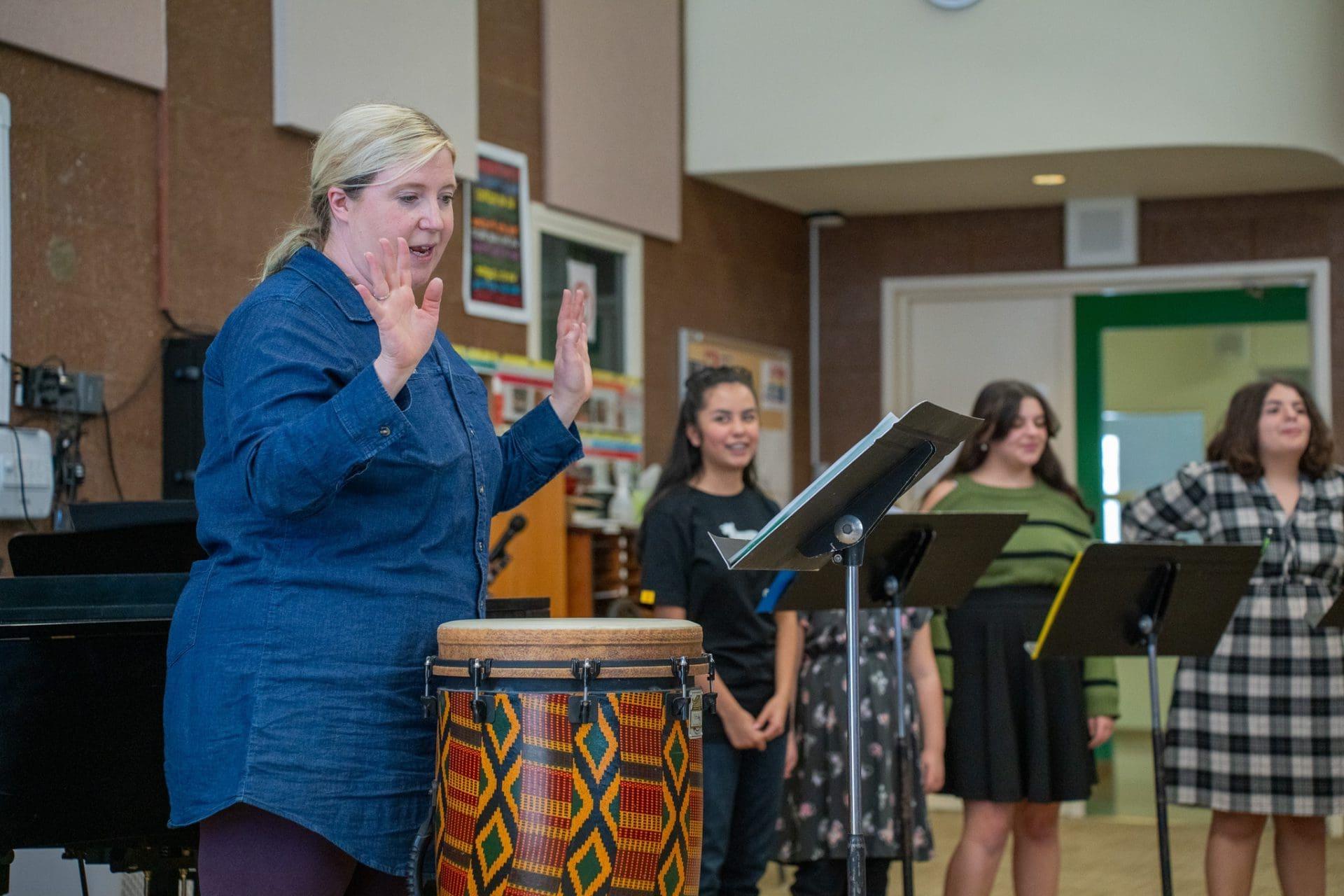 Music teacher conducting choir rehearsal with students.